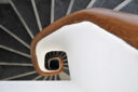 Wooden handrail of a staircase spirals down amidst radiating treads