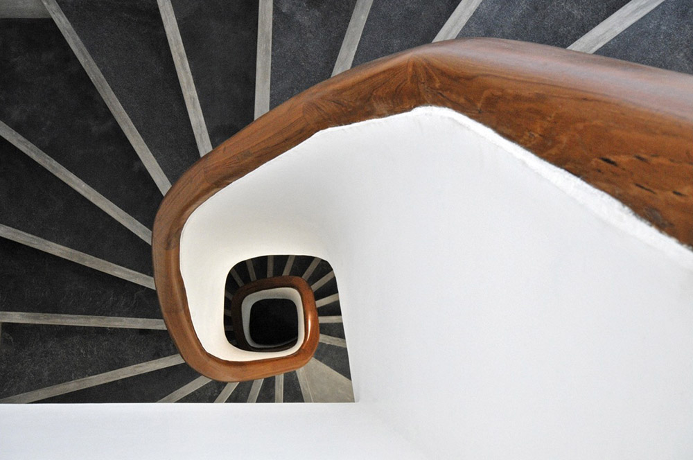 Wooden handrail of a staircase spirals down amidst radiating treads